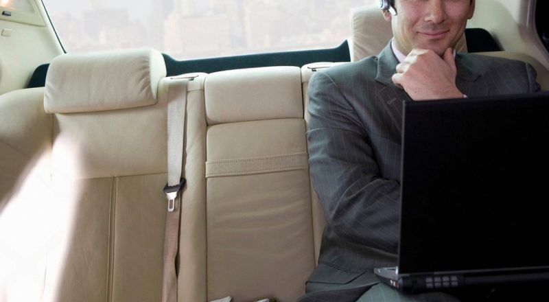Business traveller working on a laptop in the back seat of a chauffeur-driven car in the UAE