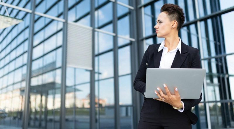 Woman in business suit holding a laptop outside a corporate building in the UAE